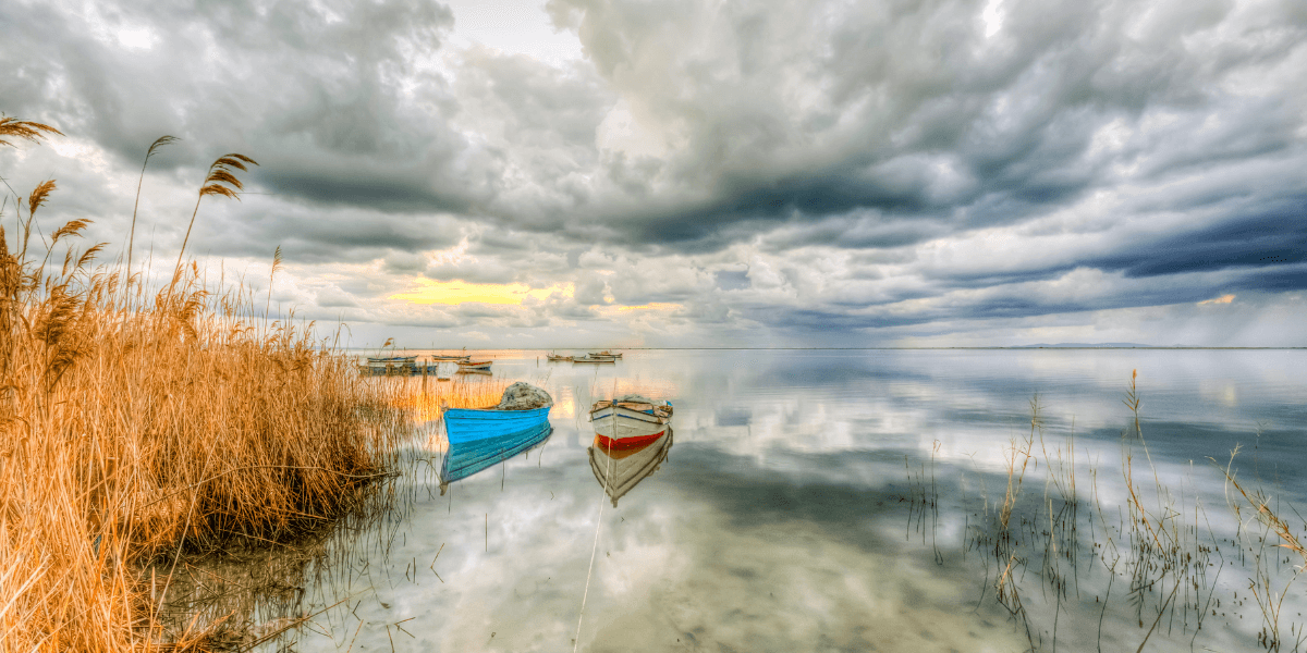 Serene lake scene with anchored boats and dramatic cloudy skies reflecting on water