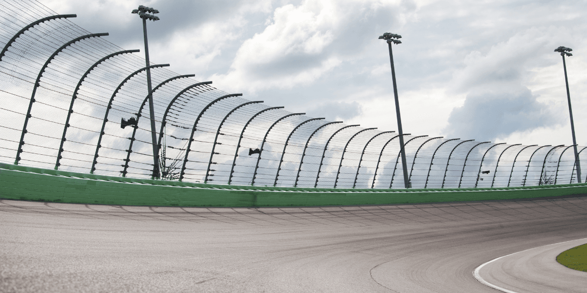 A smooth racetrack curves towards a protective fence under a cloudy sky