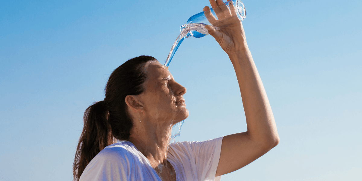 Woman pouring water over her head against a clear blue sky