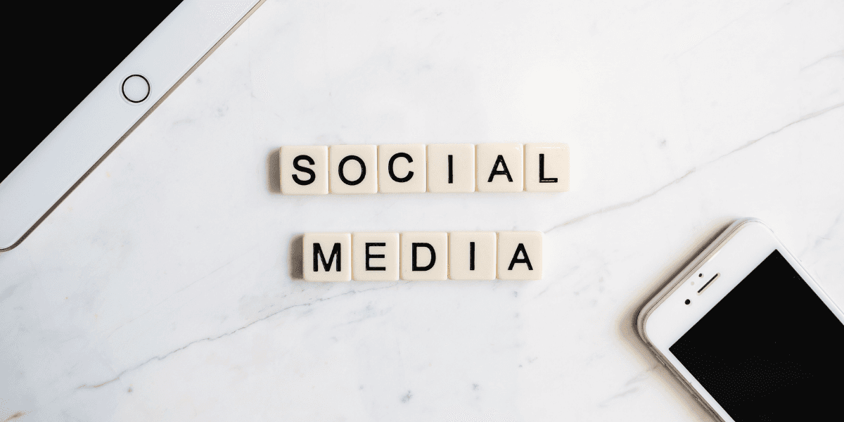Scrabble tiles spelling "SOCIAL MEDIA" on a marble surface with smartphones nearby