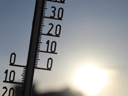 Outdoor thermometer silhouetted against bright sunlight during hot weather.