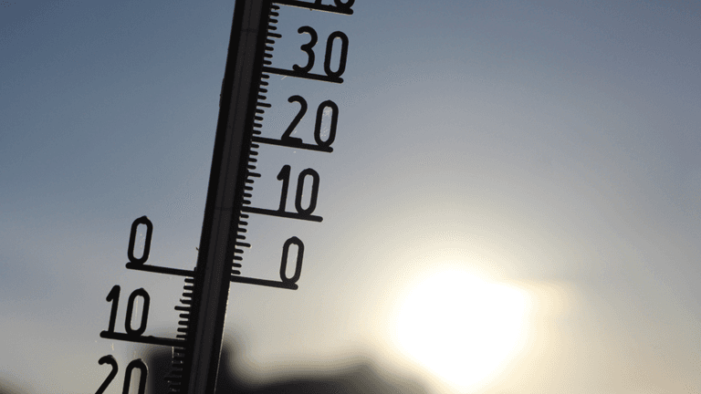 Outdoor thermometer silhouetted against bright sunlight during hot weather.