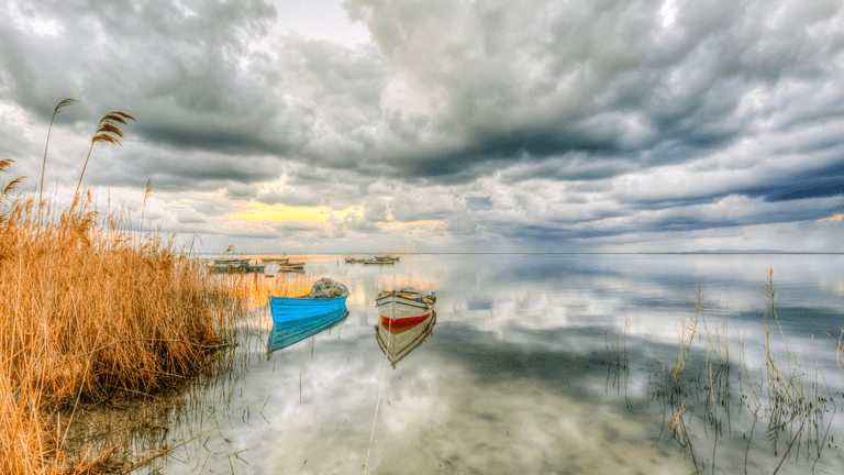 Serene lake scene with anchored boats and dramatic cloudy skies reflecting on water