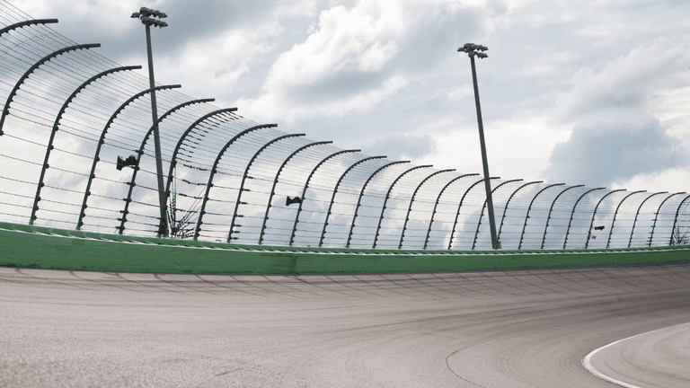 A smooth racetrack curves towards a protective fence under a cloudy sky