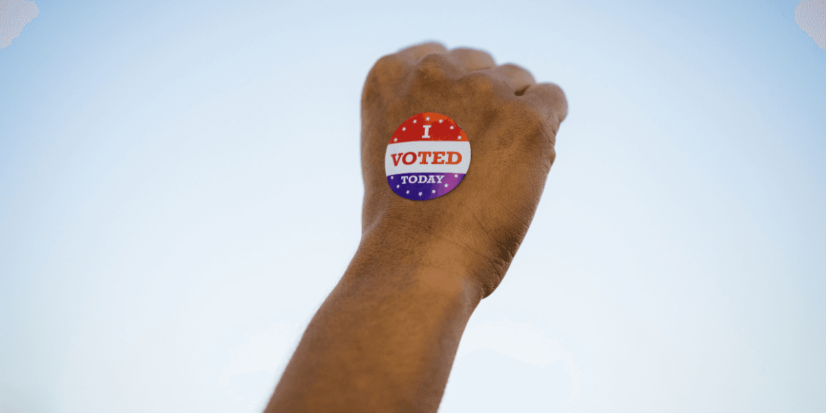 A hand with an "I Voted Today" sticker against a clear sky backdrop