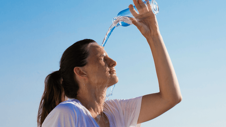 Woman pouring water over her head against a clear blue sky