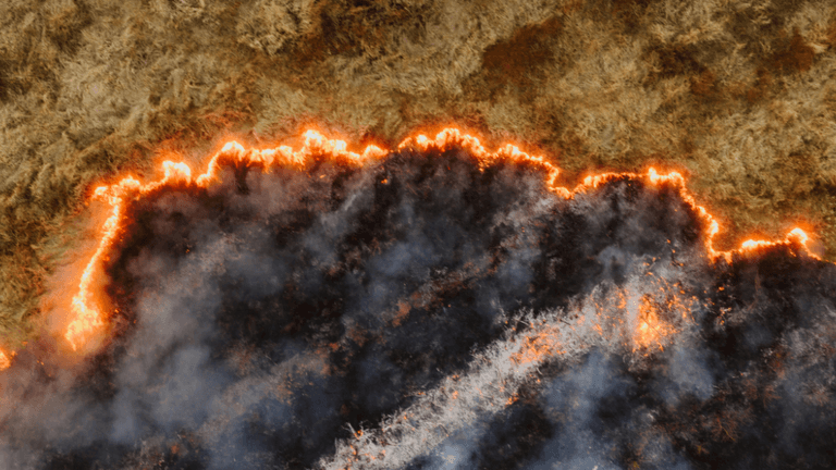 Aerial view of a wildfire with flames and smoke on a dry landscape.