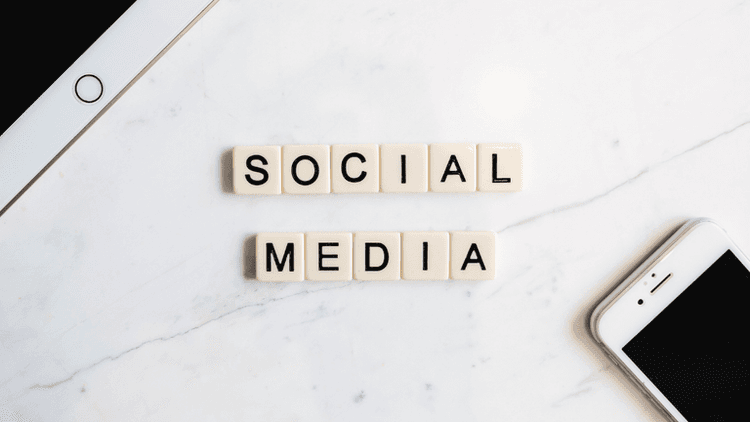 Scrabble tiles spelling "SOCIAL MEDIA" on a marble surface with smartphones nearby