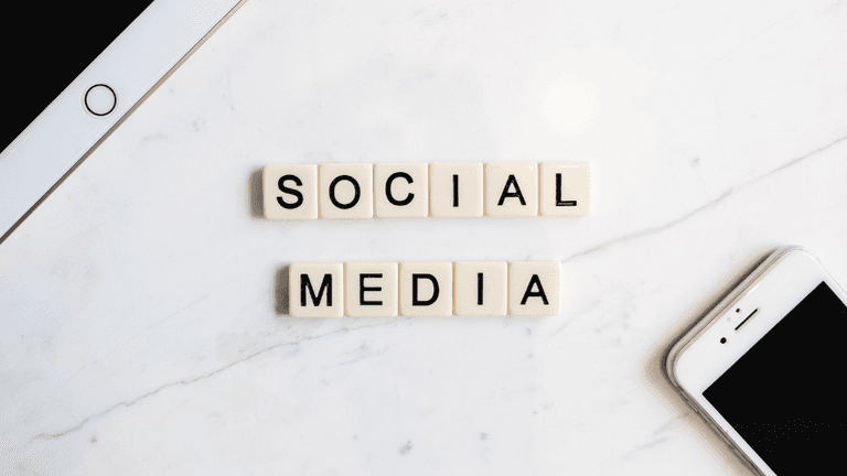 Scrabble tiles spelling "SOCIAL MEDIA" on a marble surface with smartphones nearby