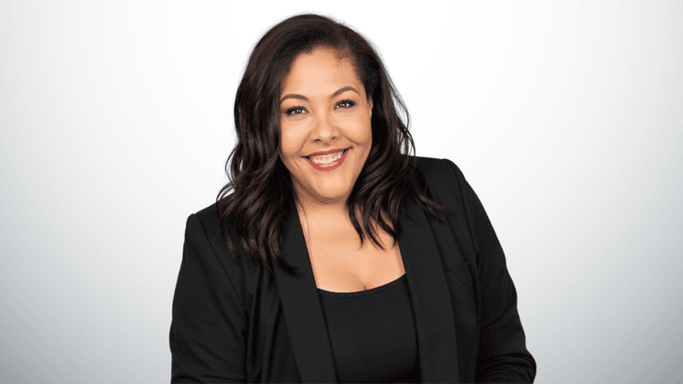 Smiling woman in a black blazer against a light gray backdrop