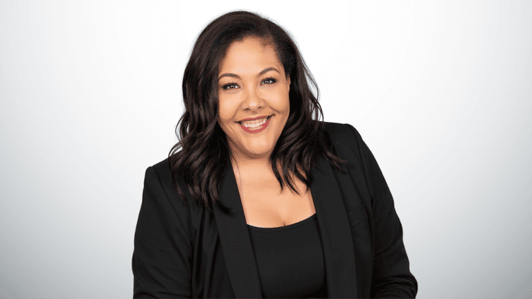 Smiling woman in a black blazer against a light gray backdrop