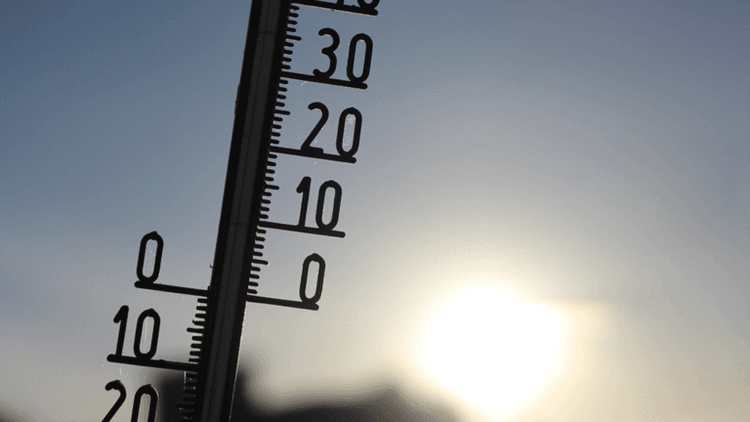 Outdoor thermometer silhouetted against bright sunlight during hot weather.