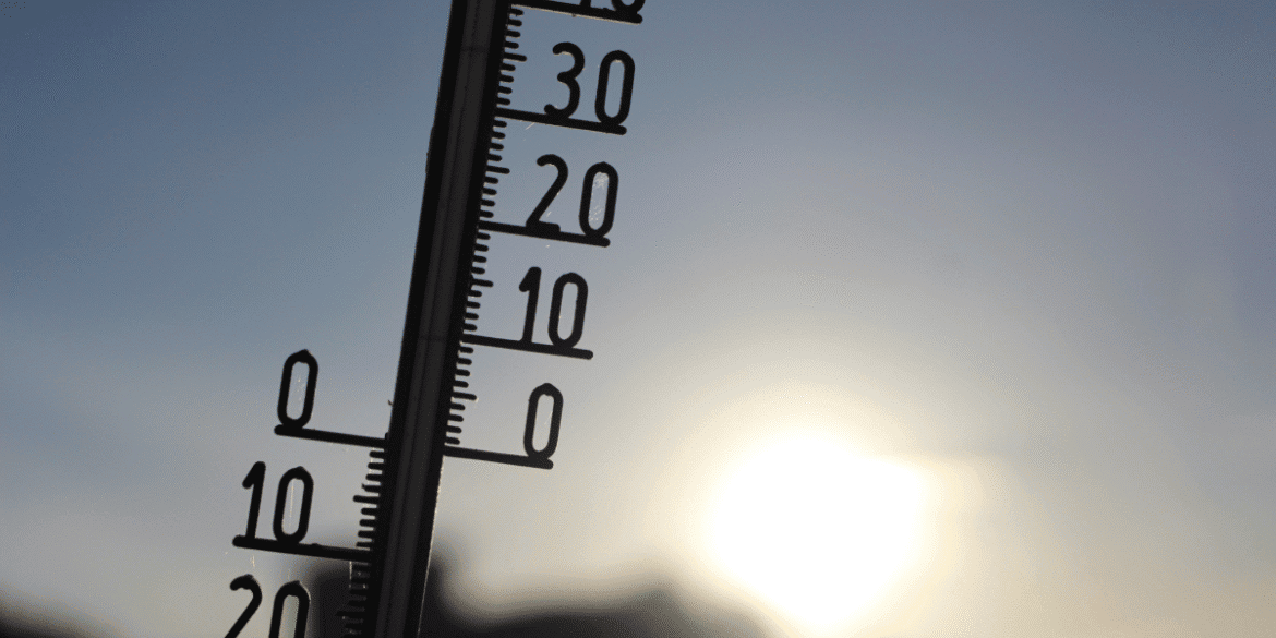 Outdoor thermometer silhouetted against bright sunlight during hot weather.